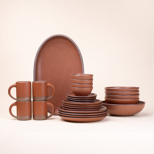 A 26-piece tablesetting with four mugs, four cake plates, four side plates, four dinner plates, 4 shallow bowls, 4 ice cream bowls, a large shallow bowl and an oval platter in a cool terracotta color