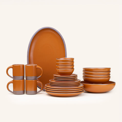 A 26-piece tablesetting with four mugs, four cake plates, four side plates, four dinner plates, 4 shallow bowls, 4 ice cream bowls, a large shallow bowl and an oval platter in an earthy orange color.