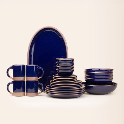 A 26-piece tablesetting with four mugs, four cake plates, four side plates, four dinner plates, 4 shallow bowls, 4 ice cream bowls, a large shallow bowl and an oval platter in a glossy dark blue color.