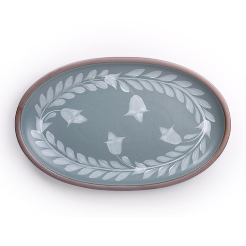 Oval ceramic platter with a hand-painted white leaf and flower border on a blue-grey background with an exposed clay rim.