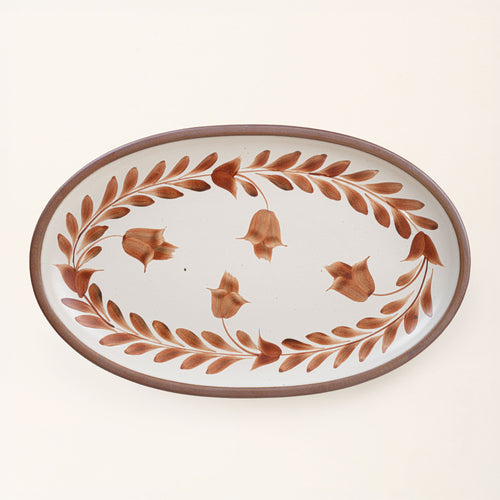 Oval ceramic platter with a hand-painted cool terracotta leaf and flower border on a cream background with an exposed clay rim.