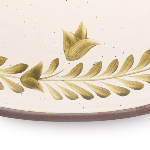 Closeup of an Oval ceramic platter with a hand-painted olive green leaf and flower border on a cream background with an exposed clay rim.