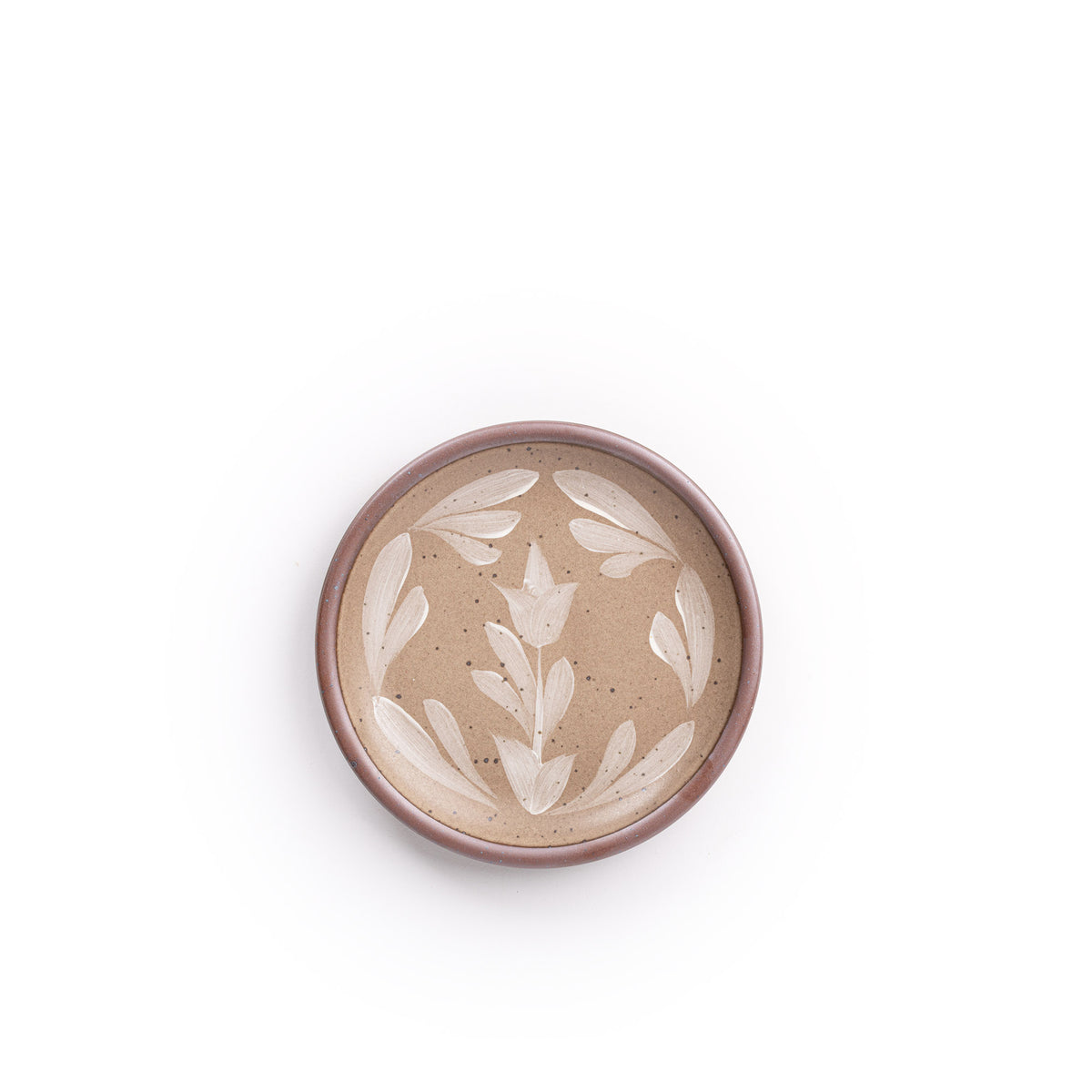 Small round ceramic plate with a hand-painted white flower and leaf design on a warm pale brown background with an exposed clay rim.