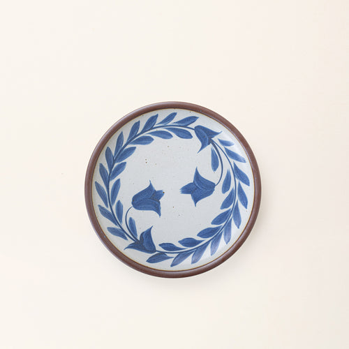 Side round ceramic plate with a hand-painted blue leaf wreath and floral design on a white background with an exposed clay rim.