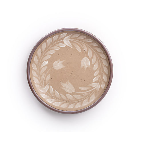 Dinner round ceramic plate with a hand-painted white leaf wreath and floral design on a warm pale brown background with an exposed clay rim.