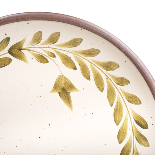 Closeup of a large round ceramic platter with a hand-painted olive green leaf wreath and floral design on a cream background with an exposed clay rim.