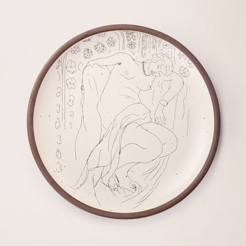 A large serving platter in a warm off-white color with unglazed rim with a black decal of the artwork, Figure endormie sur fond moucharabieh, from Henri Matisse.