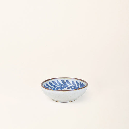 Small ceramic shallow bowl with a hand-painted blue leaf border on a white interior and speckled white exterior with an exposed clay rim.