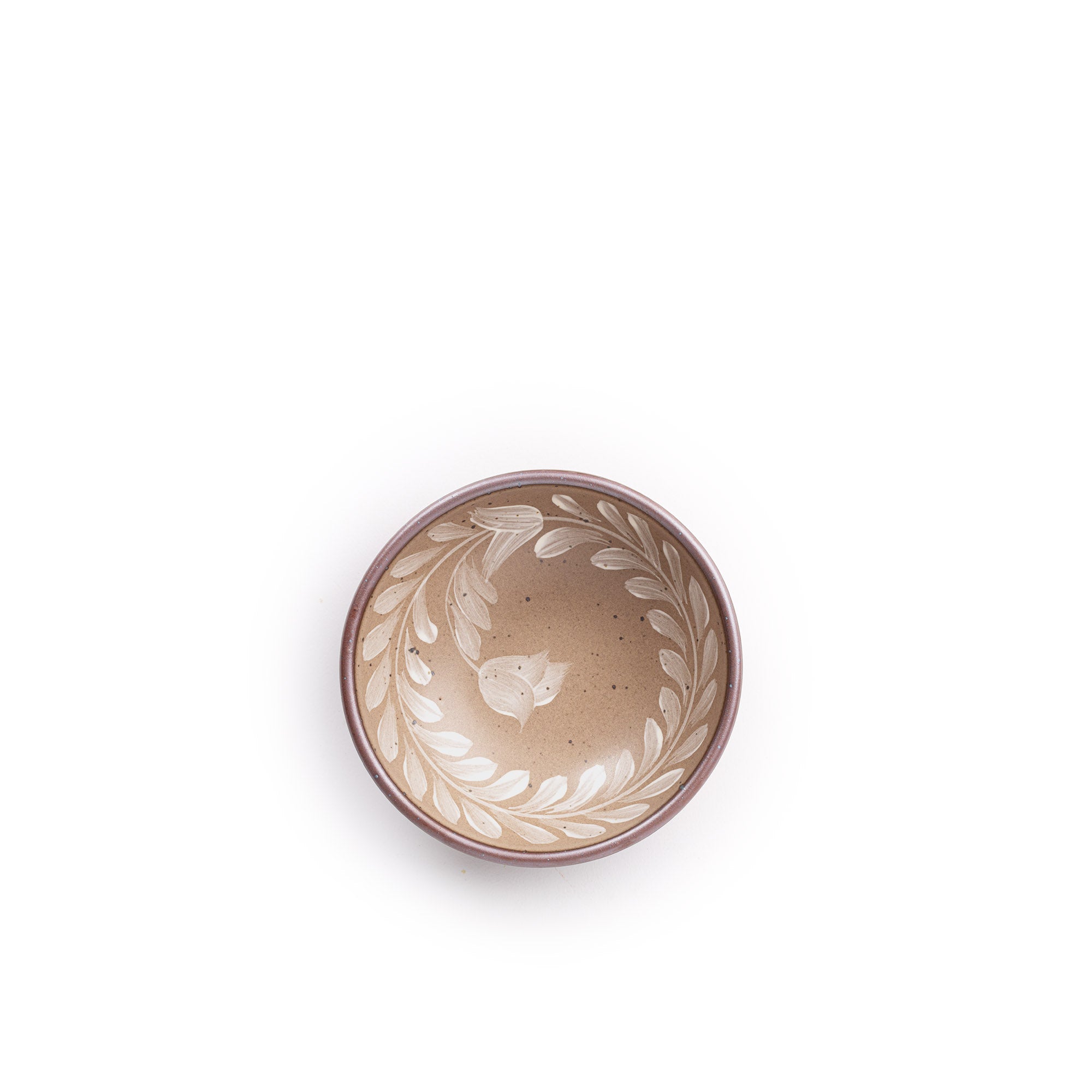 Overhead view of a small ceramic shallow bowl with a hand-painted white leaf border on a pale warm brown interior and exterior with an exposed clay rim.