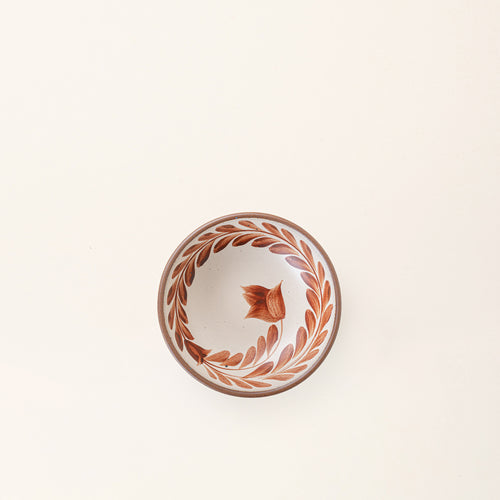 An overhead view of a Small ceramic shallow bowl with a hand-painted cool terracotta leaf border on a cream interior and speckled cream exterior with an exposed clay rim.