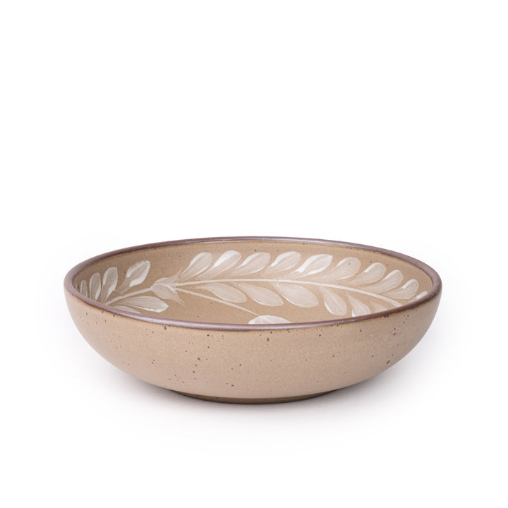 Large ceramic shallow bowl with a hand-painted white leaf border on a pale warm brown interior and exterior with an exposed clay rim.