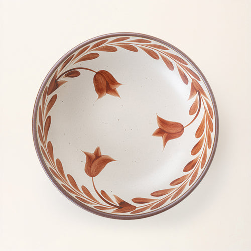 An overhead view of a large ceramic shallow bowl with a hand-painted cool terracotta leaf border on a cream interior and exterior with an exposed clay rim.