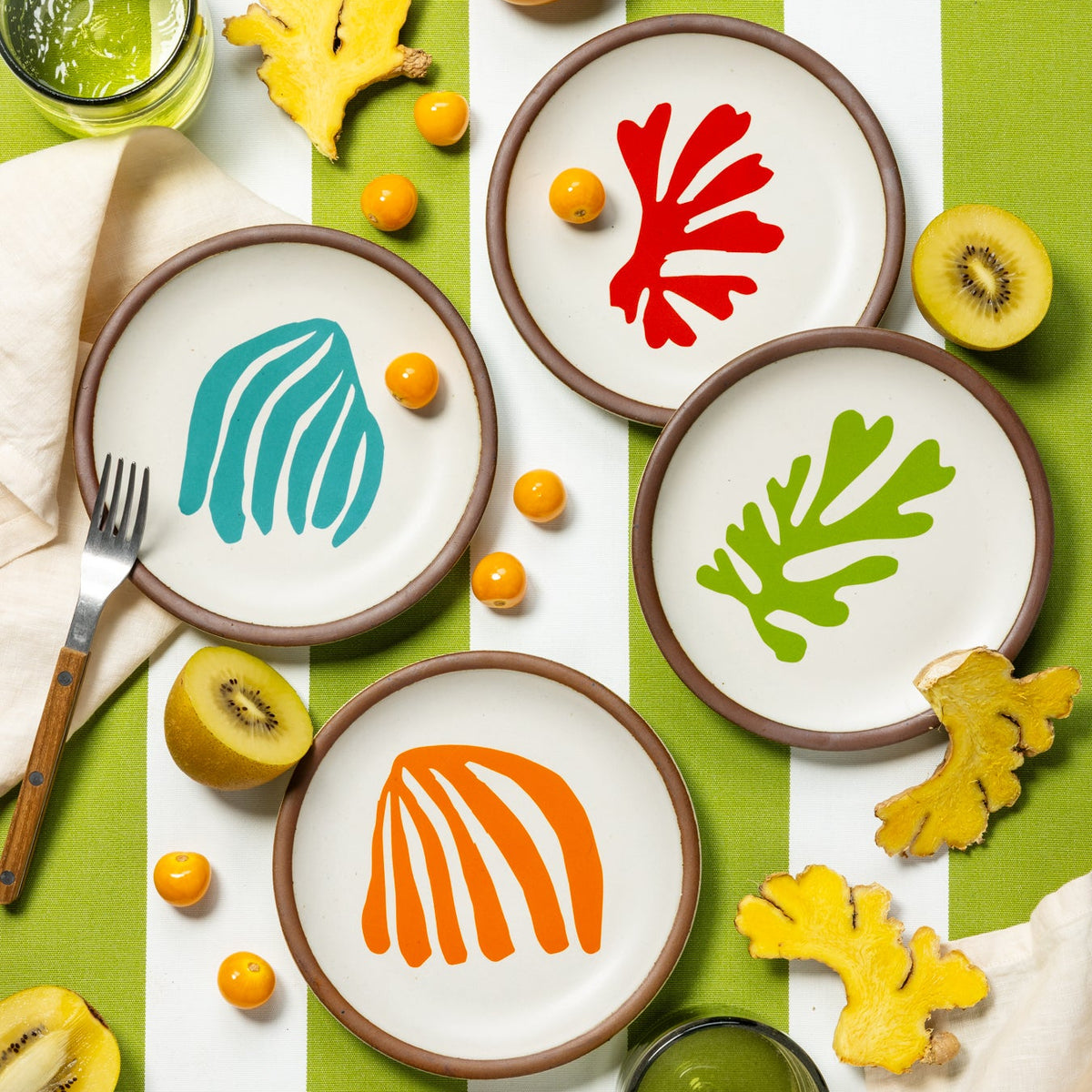 An overhead view of La Perruche Cake Plates styled with colorful linens and orange flowers.