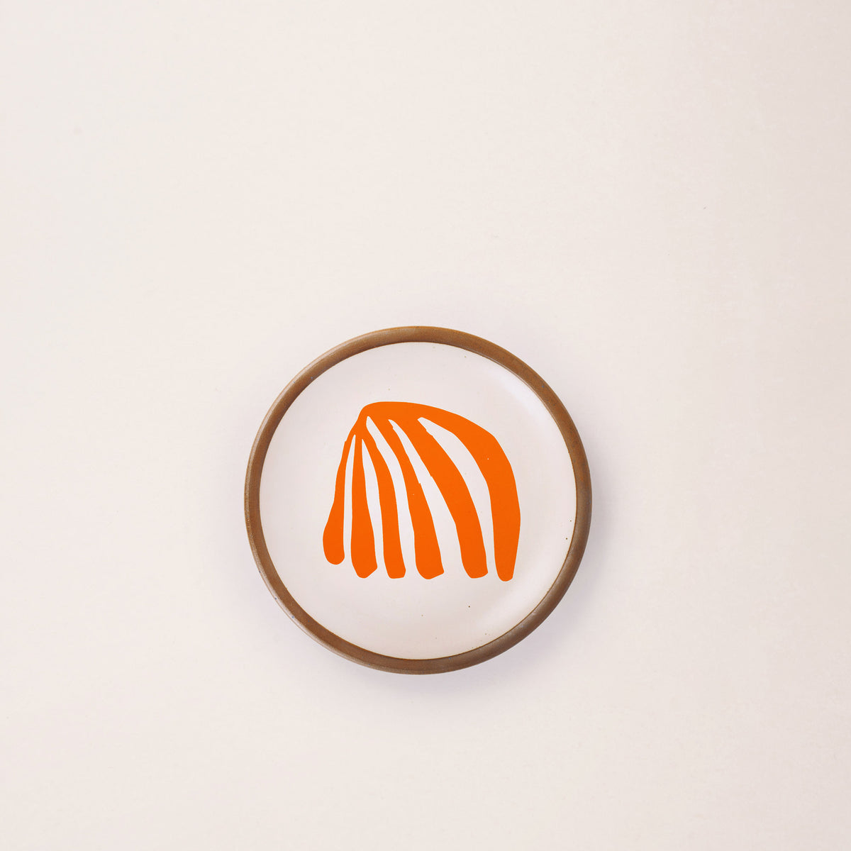 A ceramic dessert sized plate in a warm off-white color with unglazed rim, an orange frond-like cut-outs from Henri Matisse’s La Perruche et la sirène.