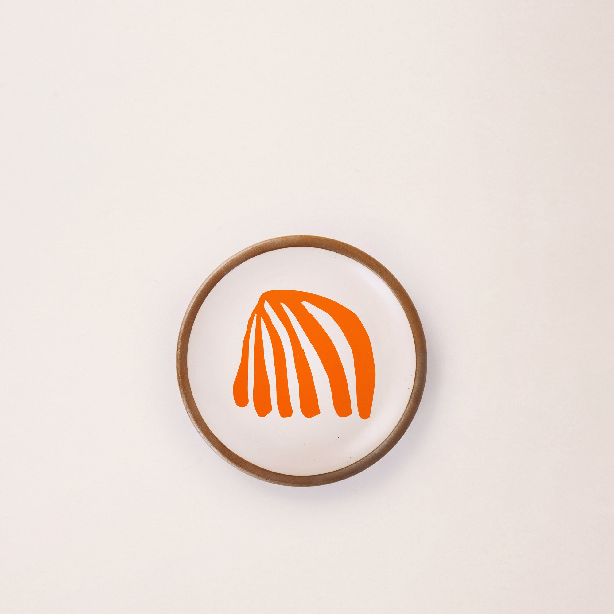 A ceramic dessert sized plate in a warm off-white color with unglazed rim, an orange frond-like cut-outs from Henri Matisse’s La Perruche et la sirène.