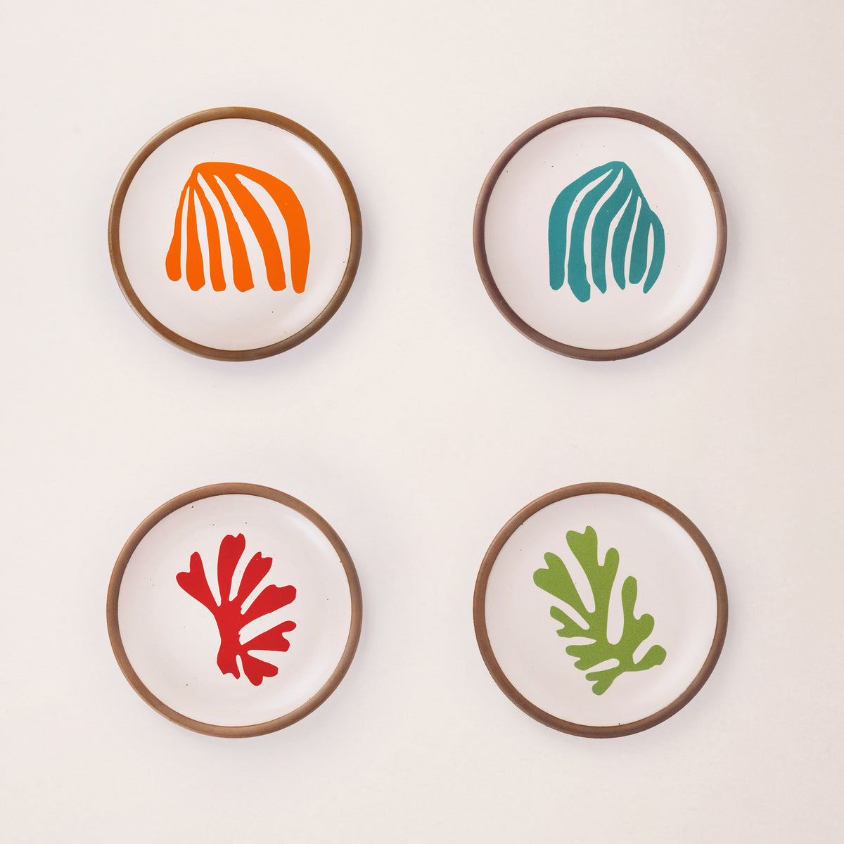 Four ceramic dessert sized plates in a warm off-white color with unglazed rim, a frond-like cut-outs from Henri Matisse’s La Perruche et la sirène.