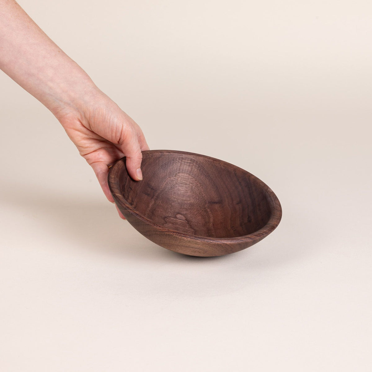 A hand holds out a small walnut wood bowl