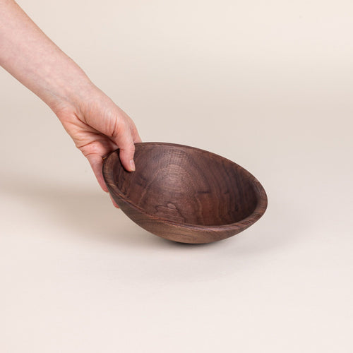 A hand holds out a small walnut wood bowl
