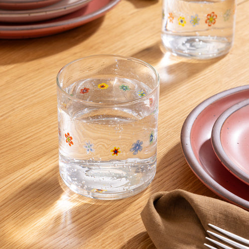 Clear glass with colorful flower pattern filled with sparkling water on a wooden table.