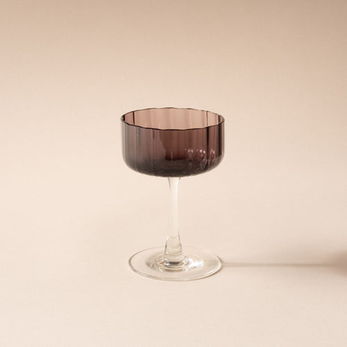 A coupe glass with a fluted bowl that is a grey purple color with a clear stem