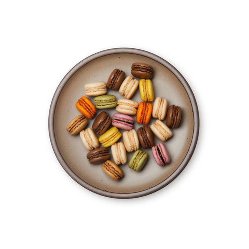 Macarons on a dinner sized ceramic plate in a warm pale brown color featuring iron speckles and an unglazed rim.