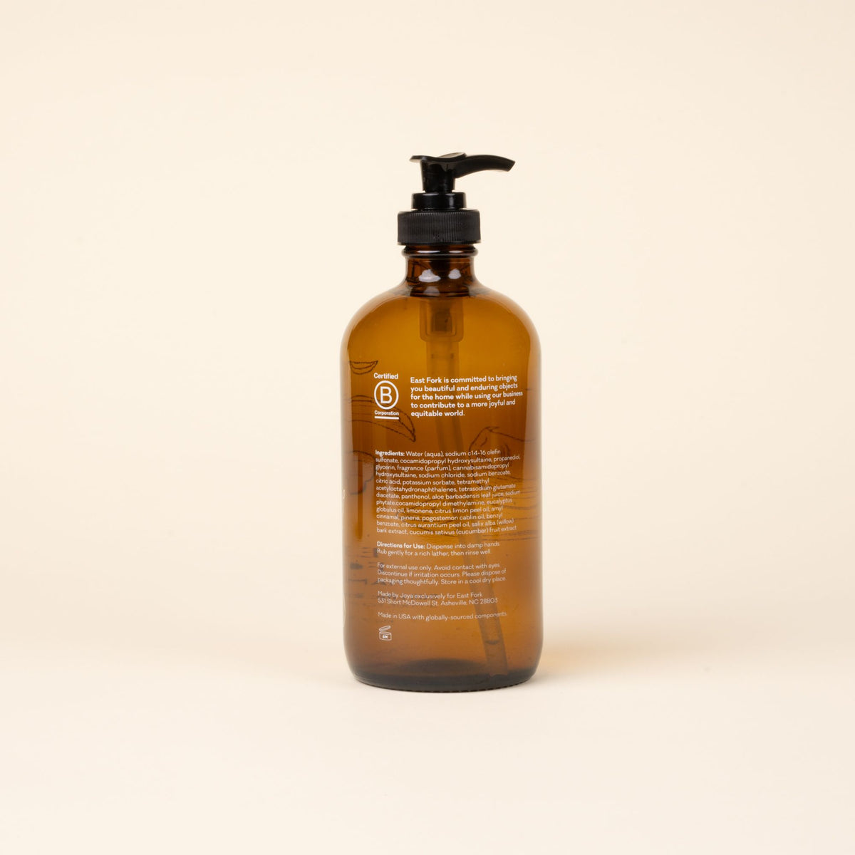 Back of amber glass pump bottle of East Fork hand soap with ingredients, centered against a light neutral background.