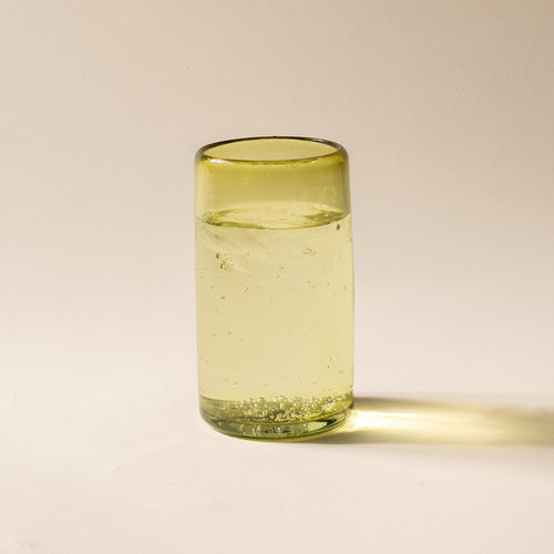 An olive green tall transparent drinking glass, filled with ice water