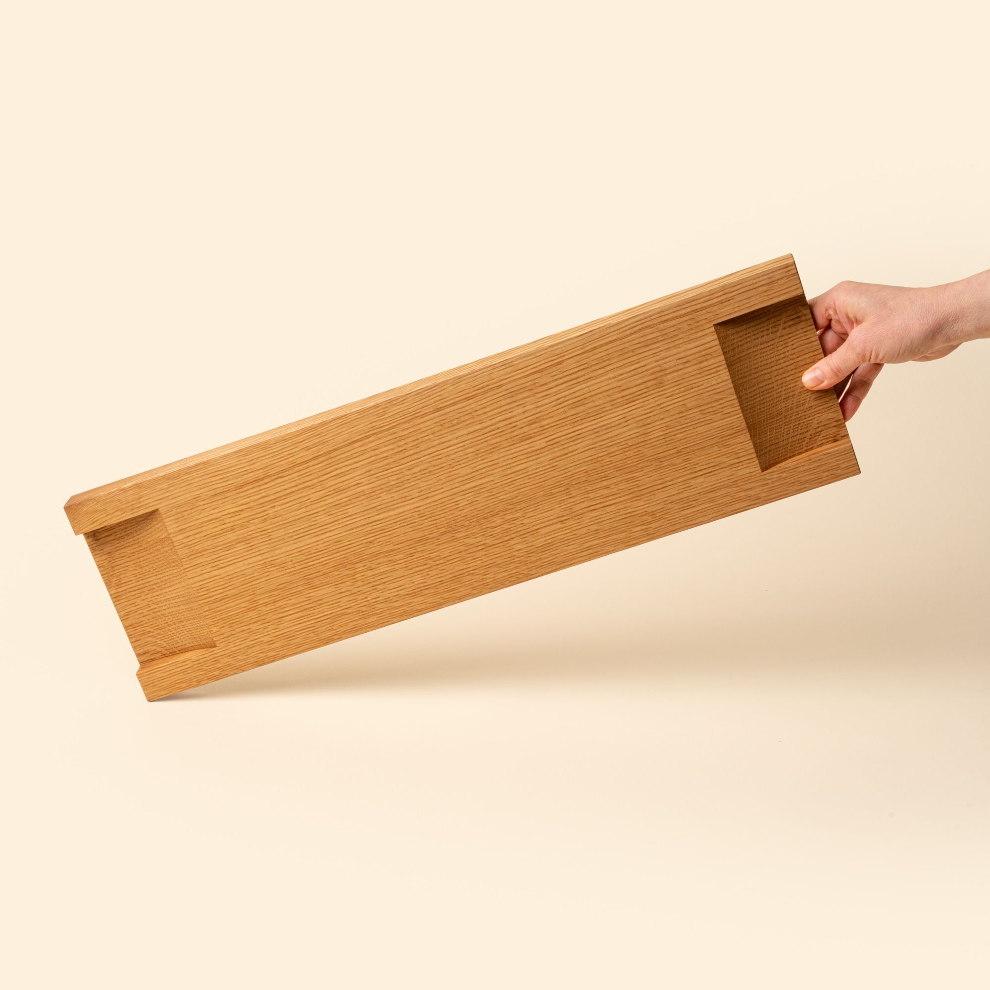 Hand holds out the back of a beveled narrow rectangle of light oak wood