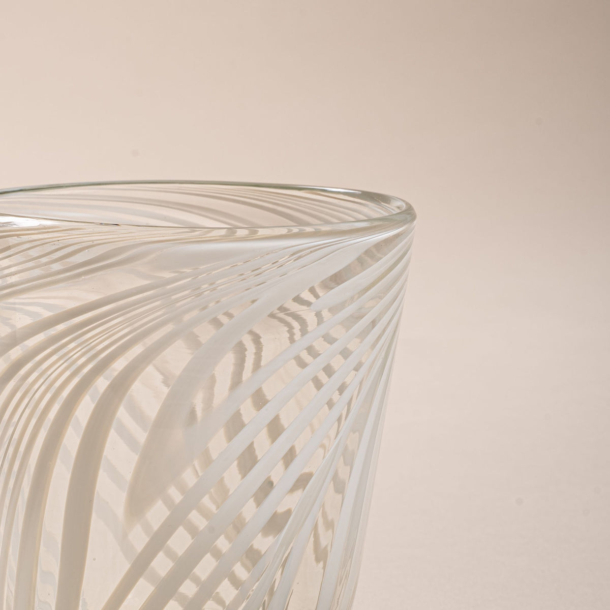 A closeup of a clear glass tumbler with white diagonal swirl pattern against a neutral background.
