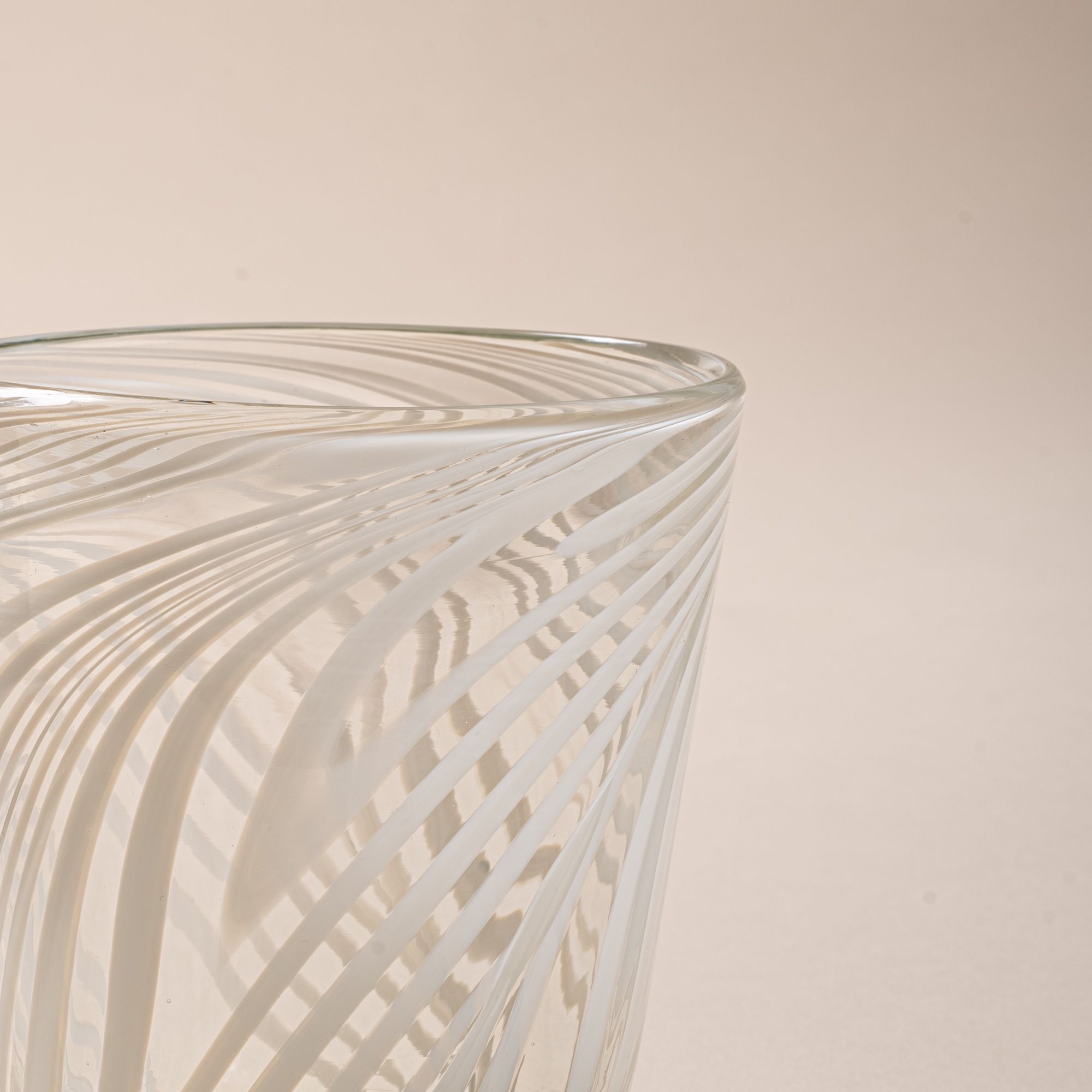 A closeup of a clear glass tumbler with white diagonal swirl pattern against a neutral background.