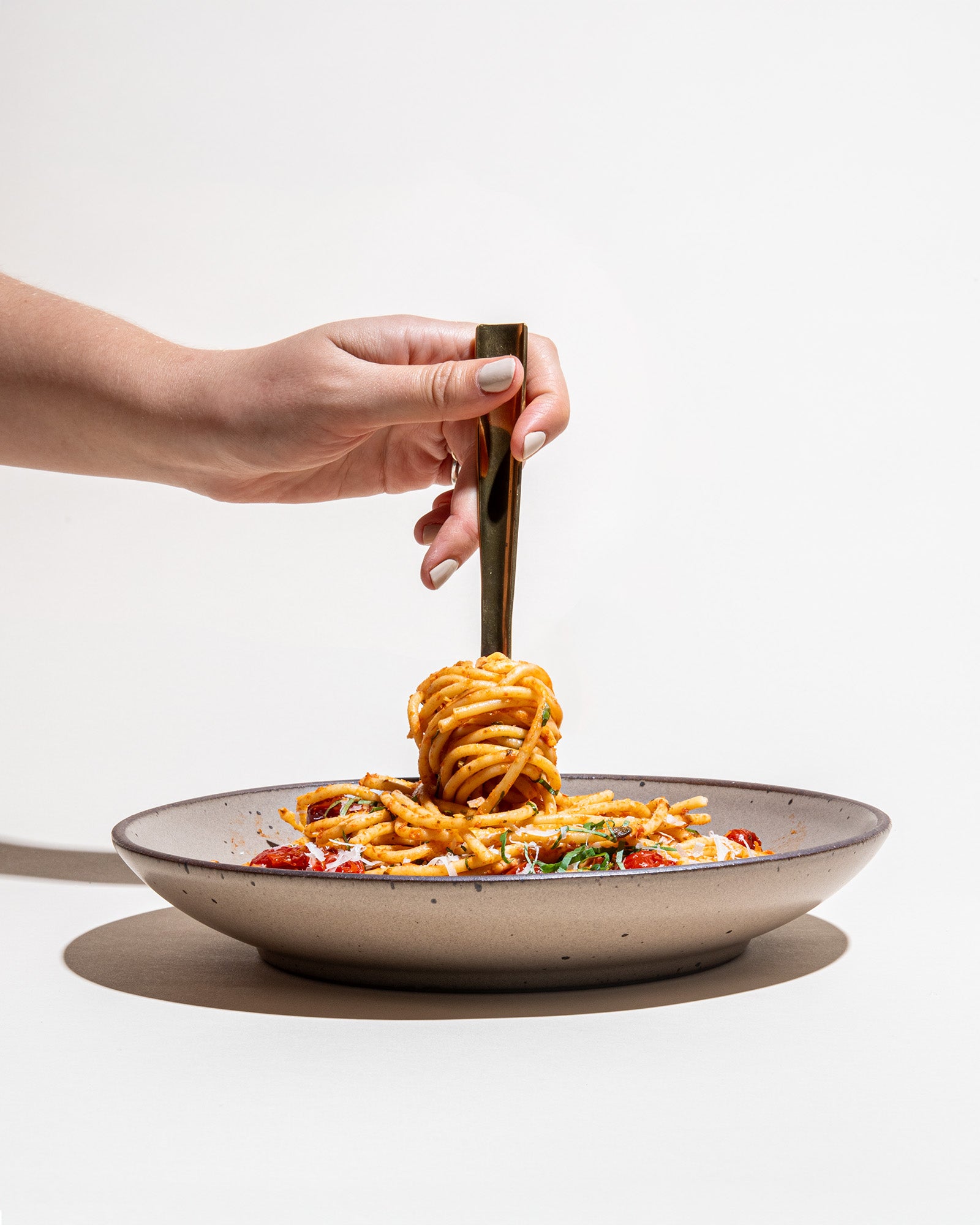 Person serving spaghetti from a coupe with a fork on a white background