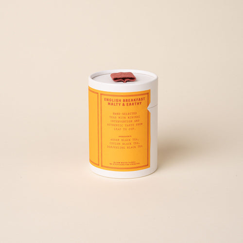 RAAZI English Breakfast tea tin with a bright orange label and red pull tab, photographed on a soft neutral backdrop.