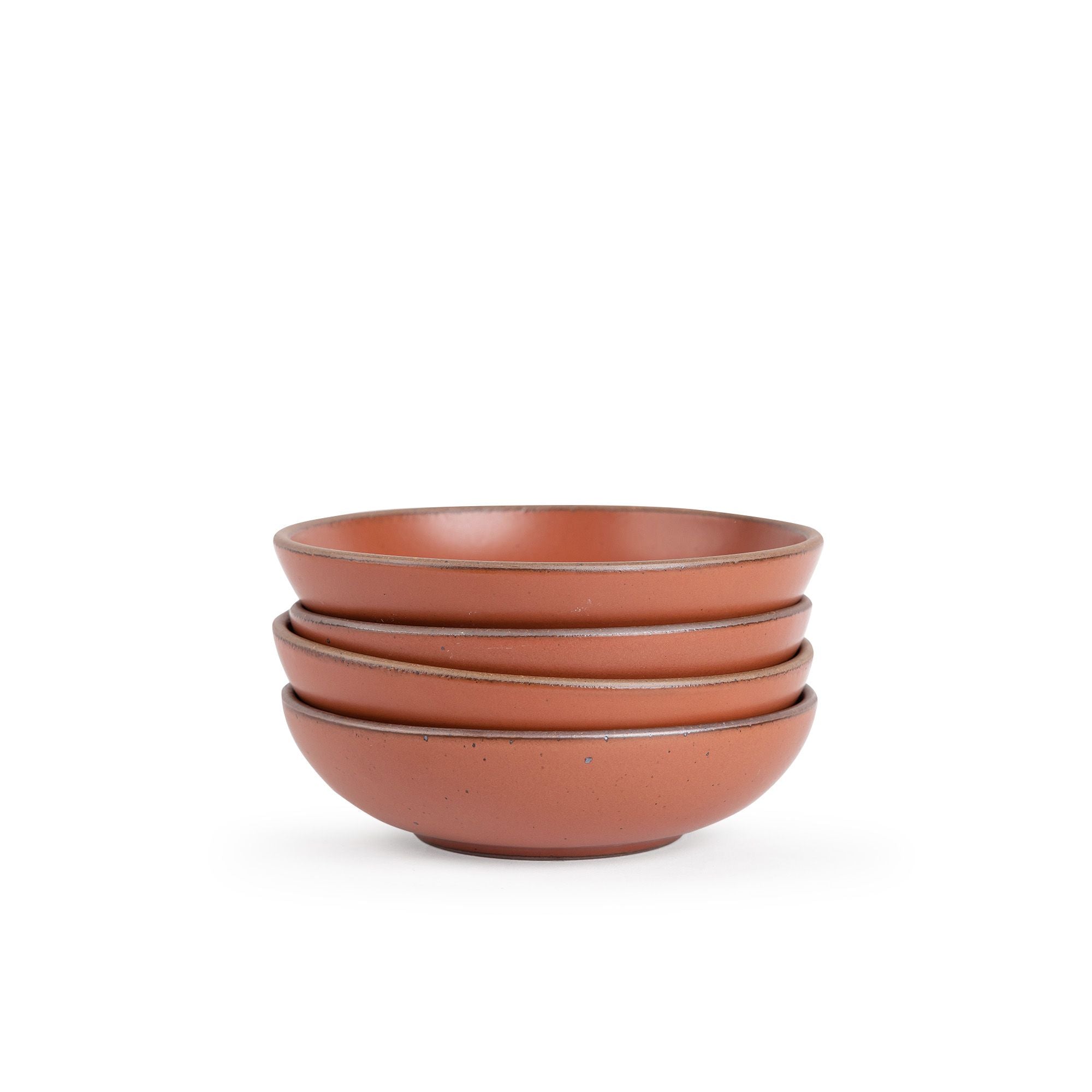 A stack of 4 dinner-sized shallow ceramic bowls in a cool burnt terracotta color featuring iron speckles and an unglazed rim