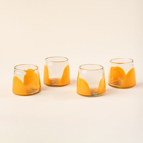 Four short clear glasses with orange arch bases arranged in a row on a light background.