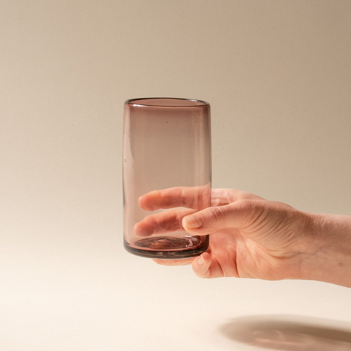 A hand holds a light plum tall transparent drinking glass
