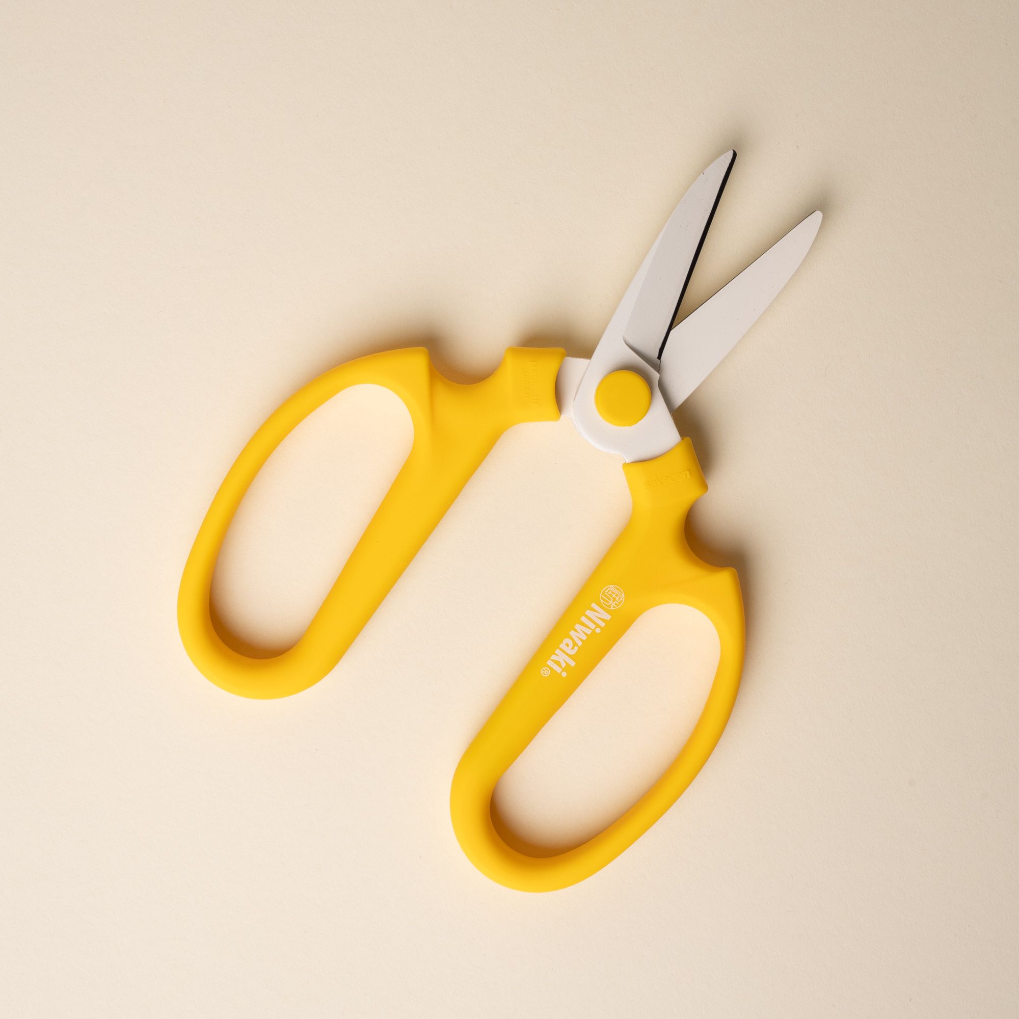 An open pair of flower scissors with large yellow handles and short blades.