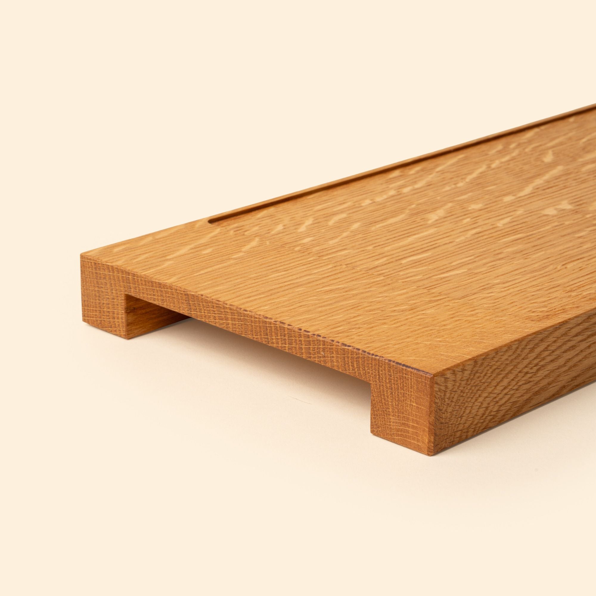 Close up of the handled edge of a narrow rectangle of light oak wood with a vertical groove at either end