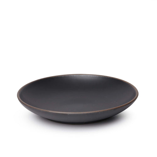 A large ceramic plate with a curved bowl edge in a graphite black color featuring iron speckles and an unglazed rim.