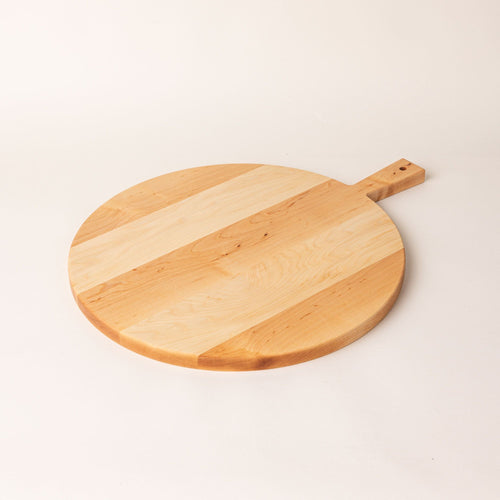 A round wooden serving board with a short rectangular handle with a hole for hanging