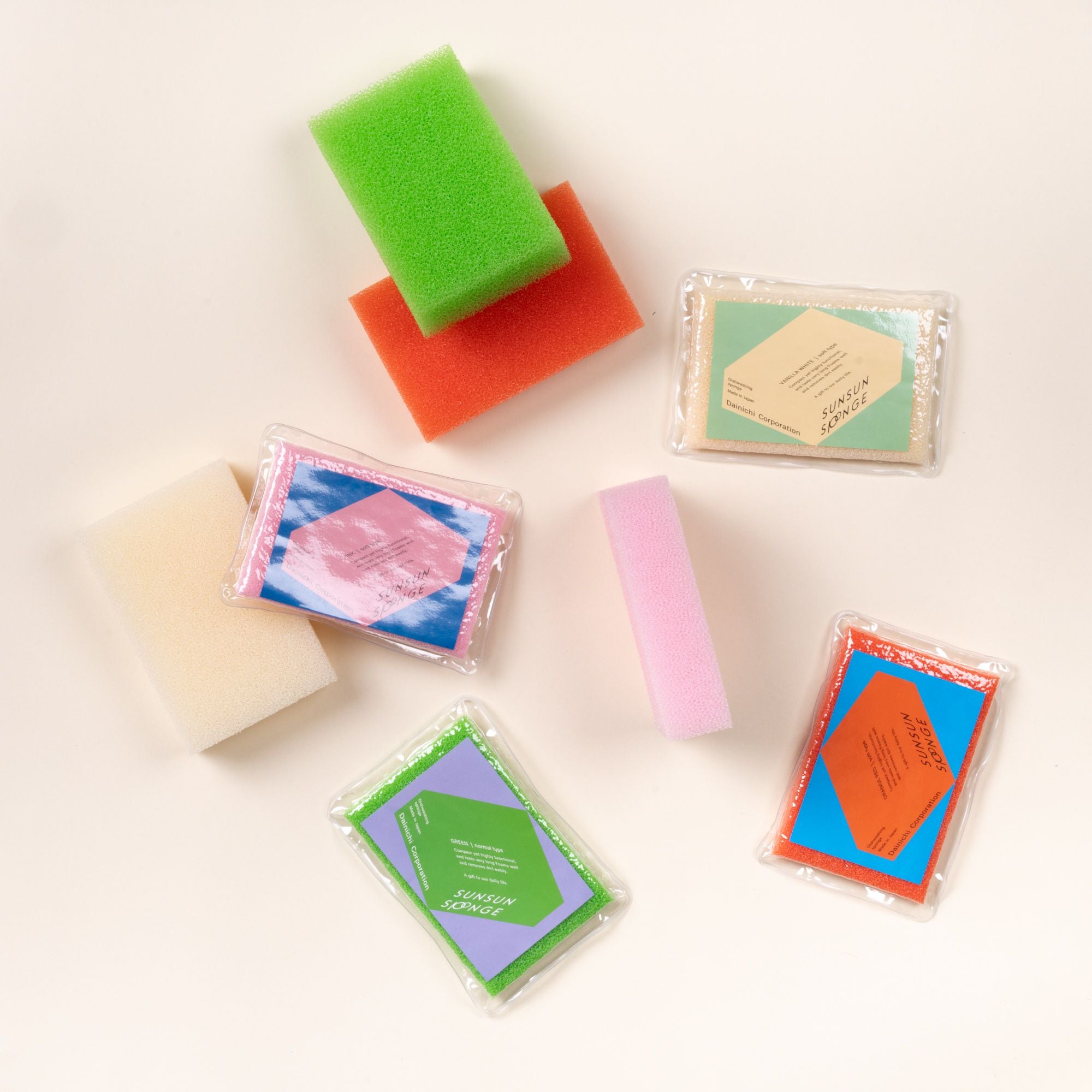 Assorted colorful dish sponges, some packaged and some loose, scattered on a light background.