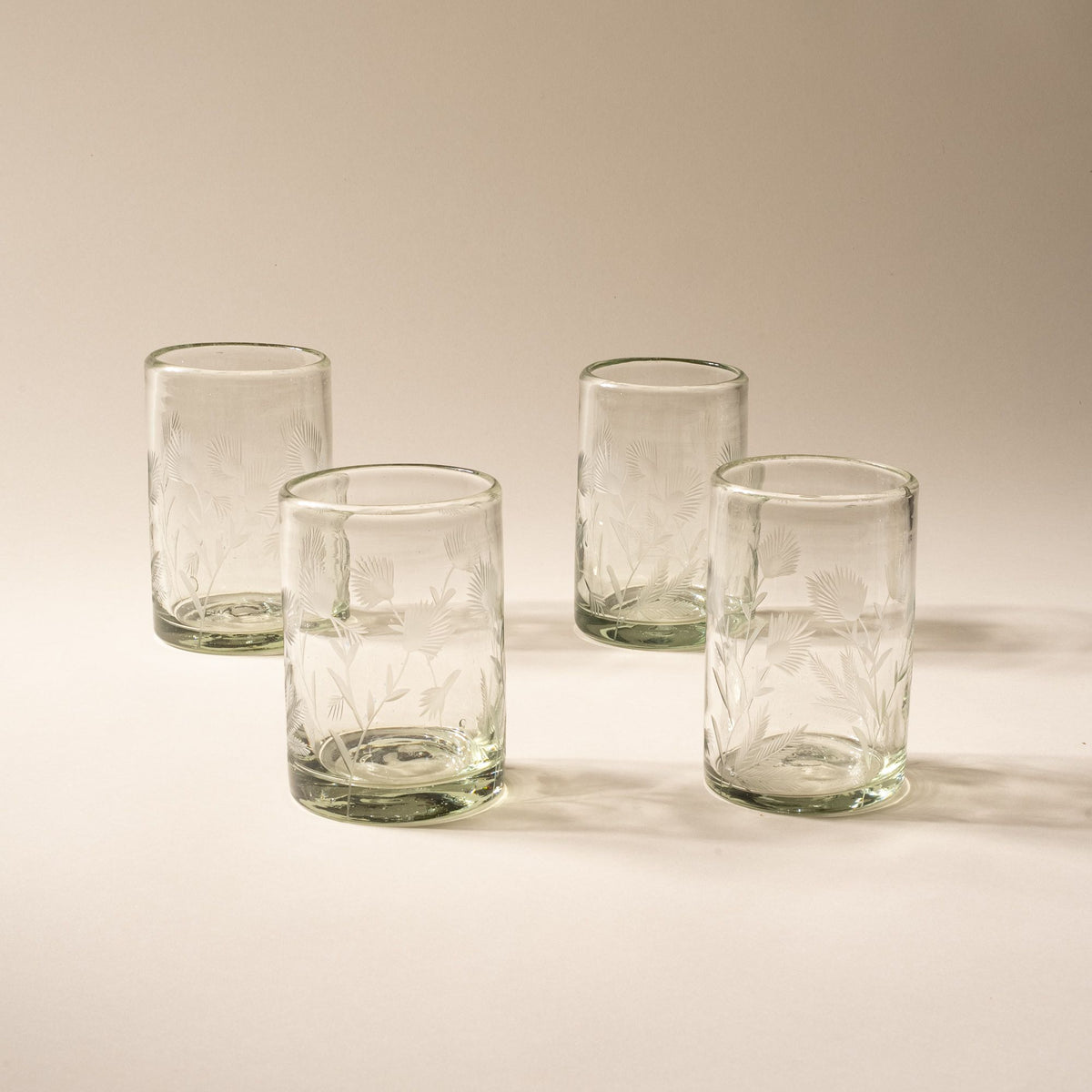 Four clear tumbler glasses made of recycled glass with etched thistle designs on it