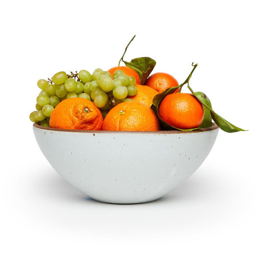 A large ceramic mixing bowl in a cool white color featuring iron speckles and an unglazed rim filled with a medley of fruit
