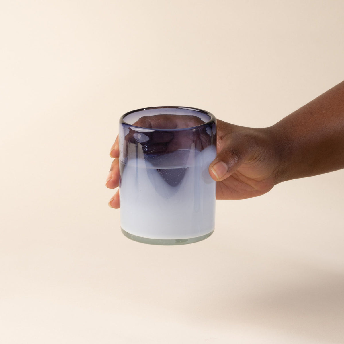 A hand holds out a white and violet handblown glass tumblers with organic wave design, with water.