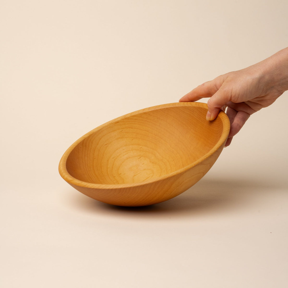 A hand holds out a medium sized round maple wood bowl