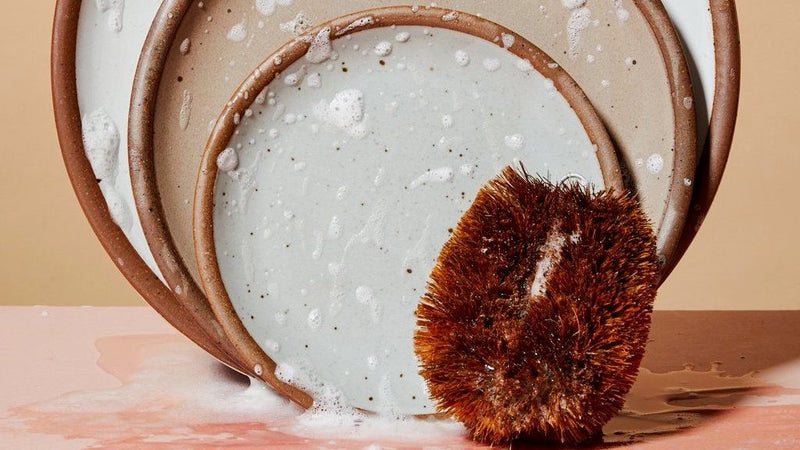 Three plates in various sizes stood on end and flecked with soap and water with a hemp fiber scrubber at lower right corner