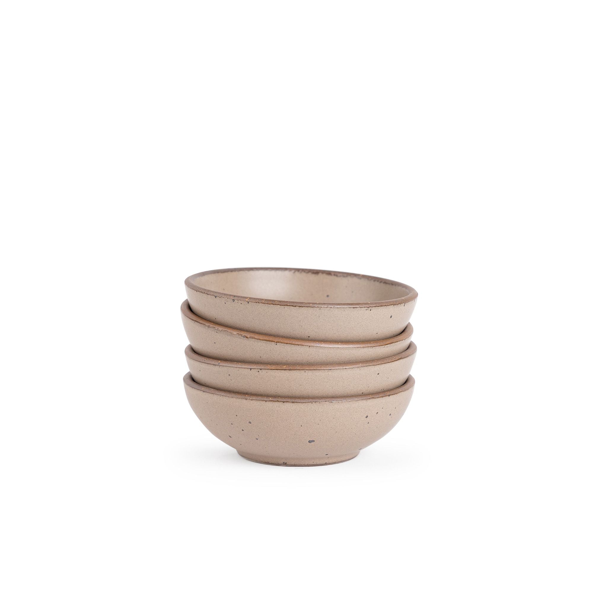 A stack of 4 small shallow ceramic bowls in a warm pale brown color featuring iron speckles and an unglazed rim