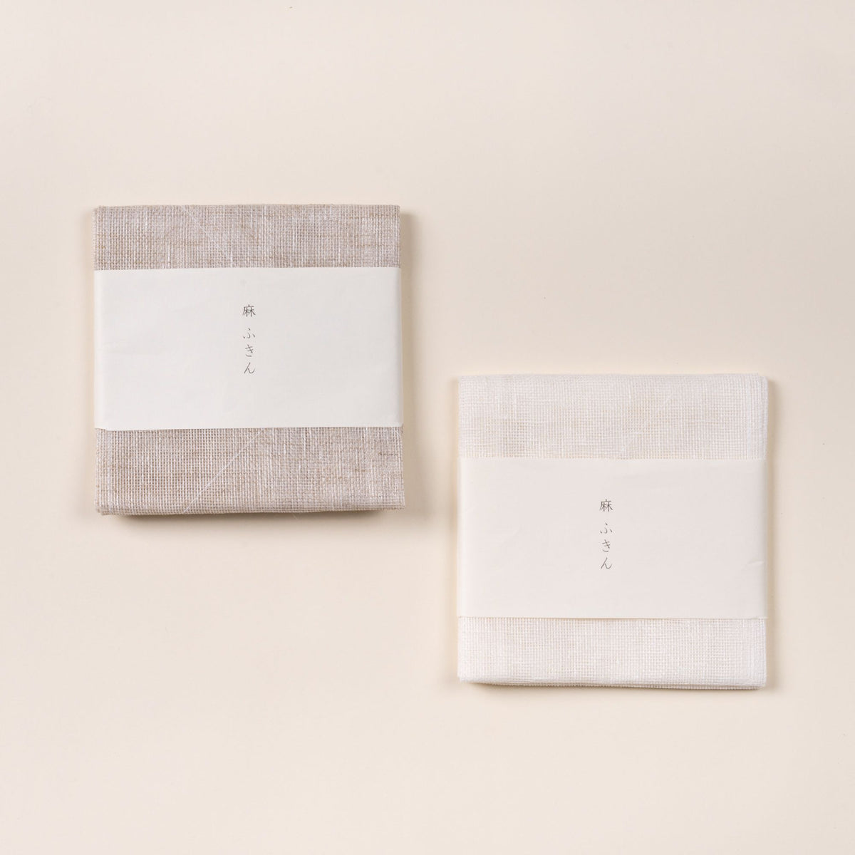 Folded white and natural color linen cleaning cloths with a white paper band featuring Japanese text, photographed on a light background.