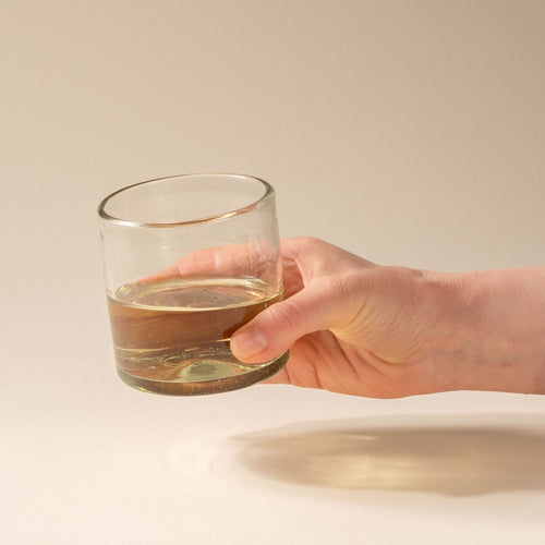 A hand holds a short clear drinking glass, filled with white wine