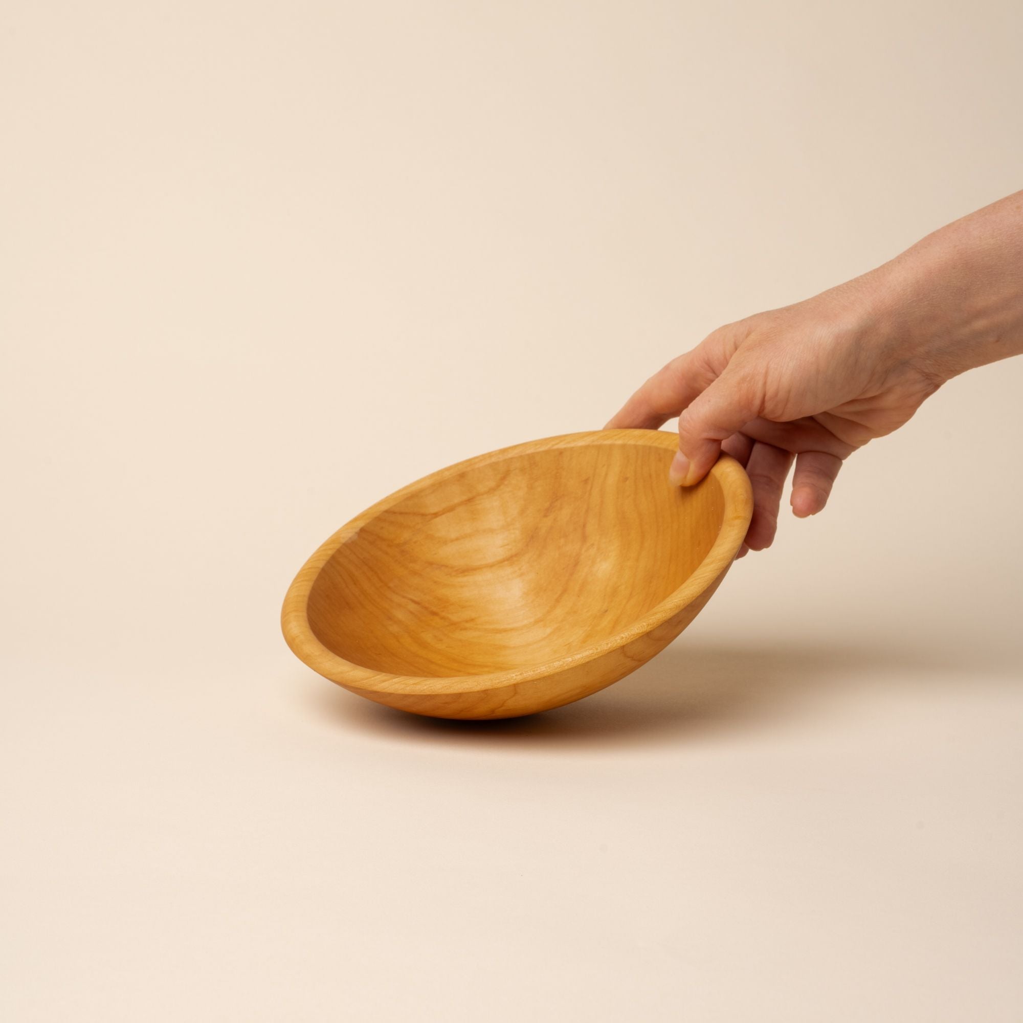 A hand holds out a small maple wood bowl