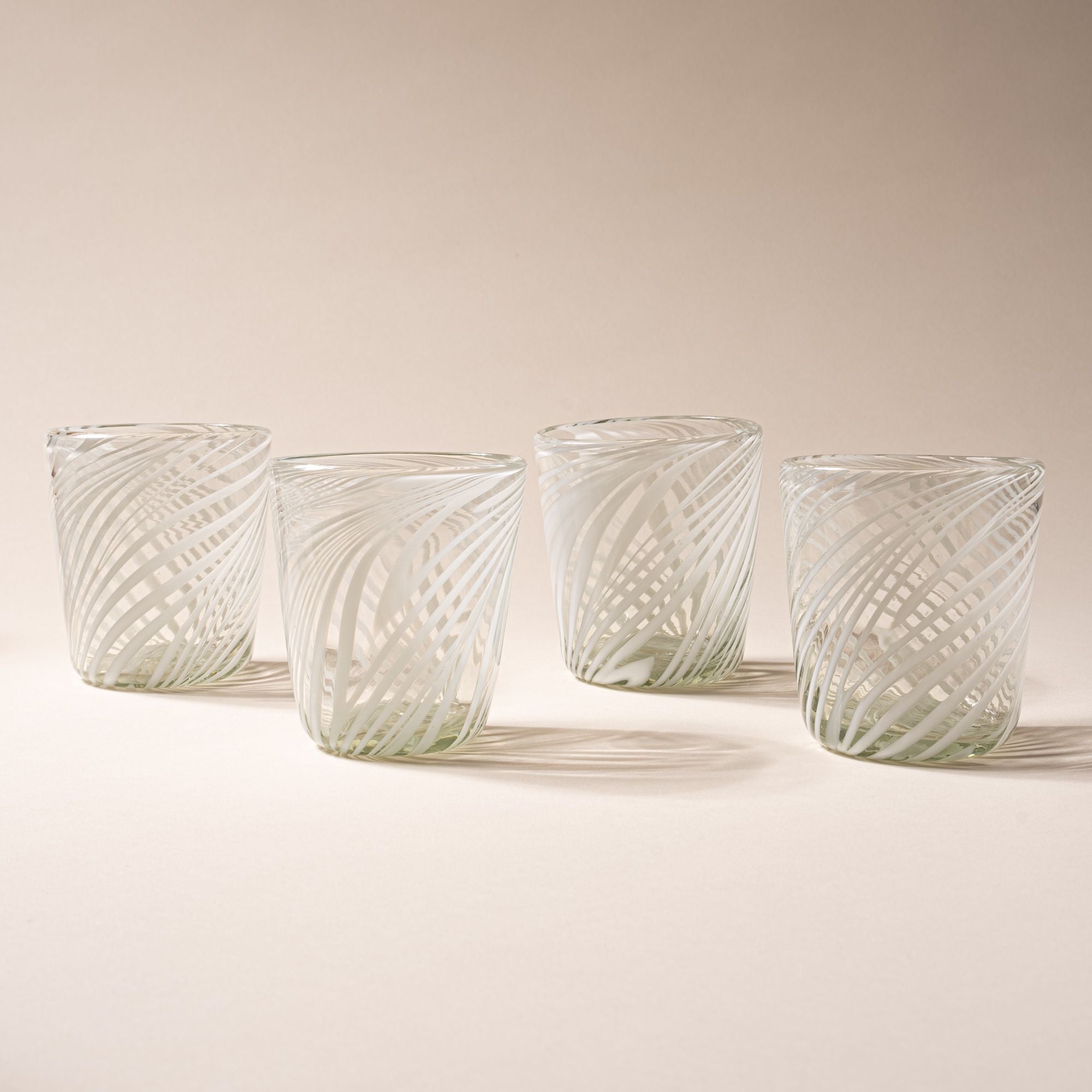 Four clear glass tumblers with white diagonal swirl pattern against a neutral background.